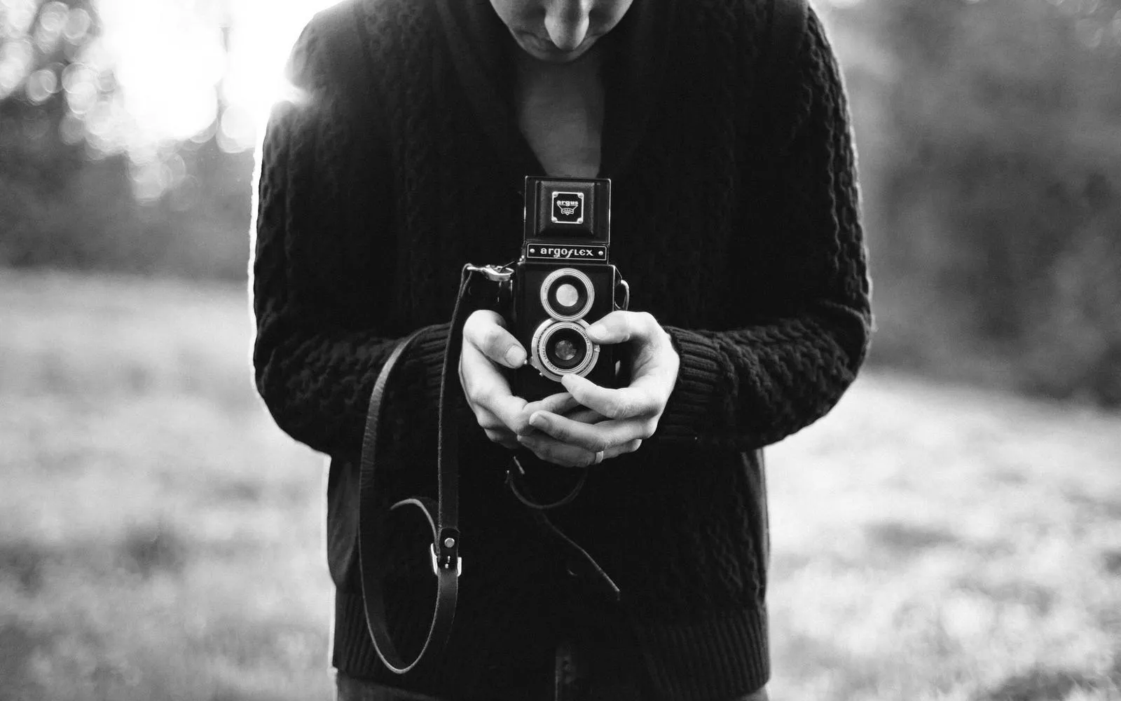 A person holding a twin-lens camera at chest height, black and white